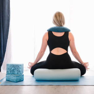 Young woman sitting on standard Yoga Bolster pillow doing meditation in Salt Lake City, UT | Santosh Yoga Institute