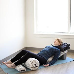 Woman relaxing on Standard Yoga Bolster pillow in Salt Lake City, UT | Santosh Yoga Institute